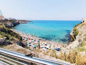 A beach with clear blue water, rocky cliffs, and umbrellas. - Your beach house in Sicily, Casa Sciàpò (Terrasini)
