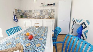 A dining area with a patterned tablecloth, blue chairs, and a white refrigerator in the background. - Your beach house in Sicily, Casa Sciàpò (Terrasini)