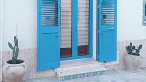 A white building with a blue door and shutters, potted plants, and a tiled entrance. - Your beach house in Sicily, Casa Sciàpò (Terrasini)