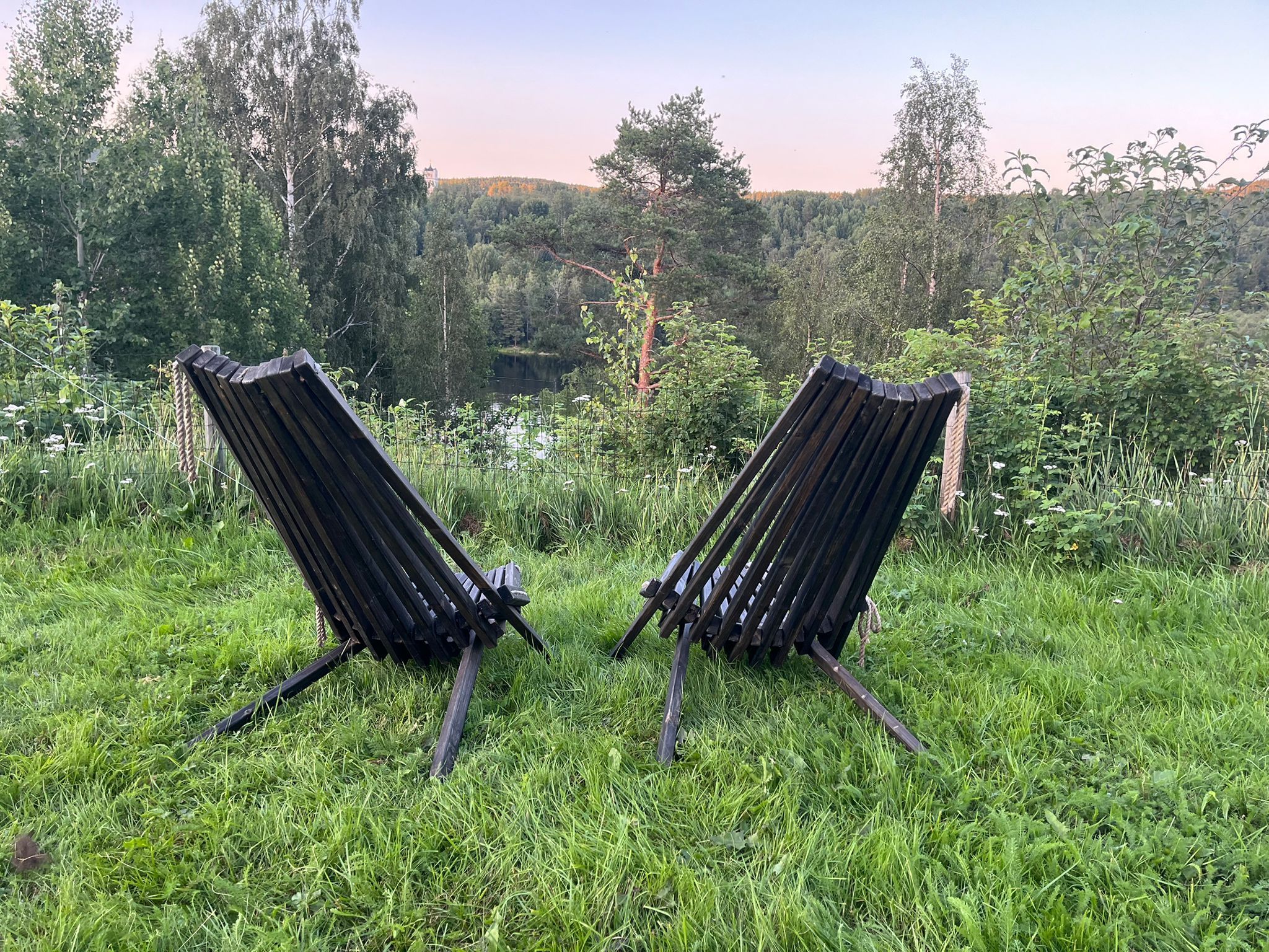 Två svarta stolar står på en gräsyta med utsikt över en skog och en kulle i bakgrunden.