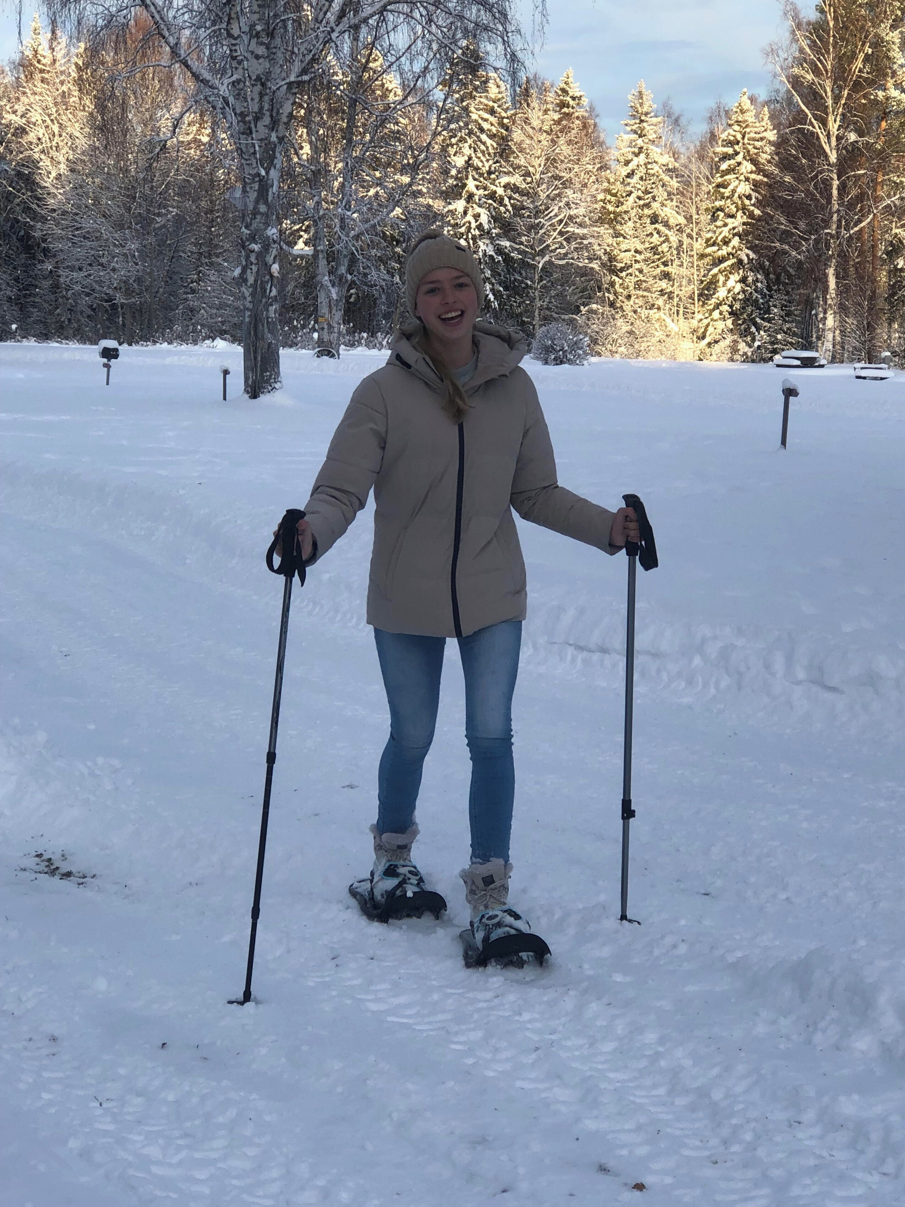 Une personne fait du ski dans un parc enneigé, avec des arbres et un ciel dégagé.