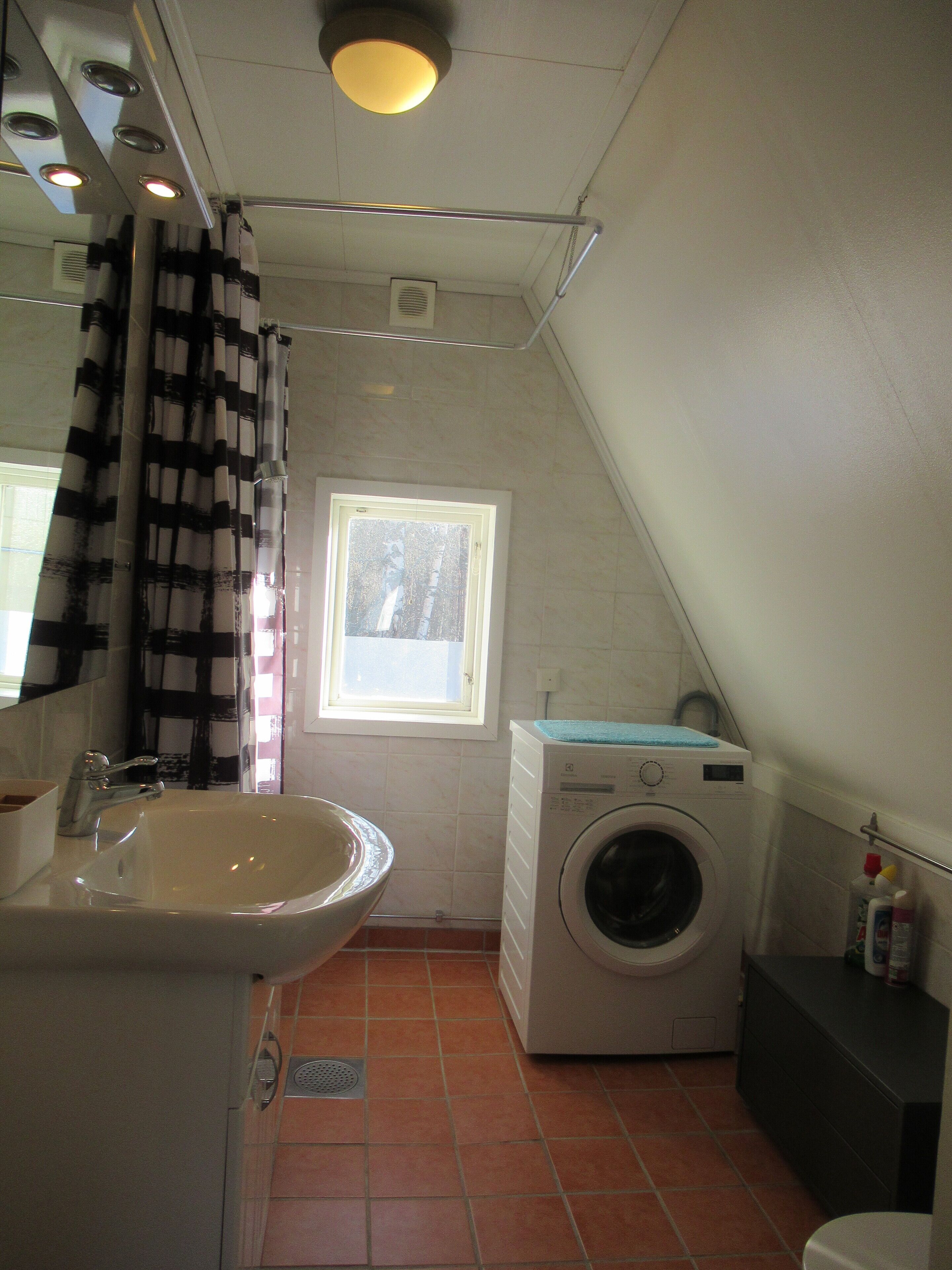 A compact laundry room with a washing machine, a sink, and a window.