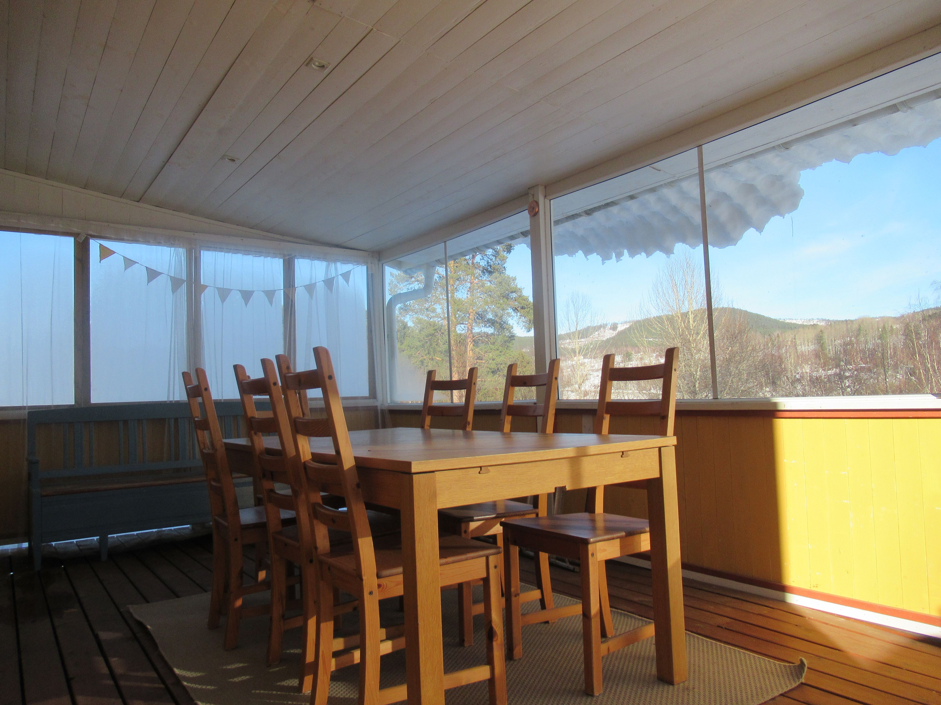 A dining area with a wooden table and chairs, large windows with curtains, and a view of a mountainous landscape.