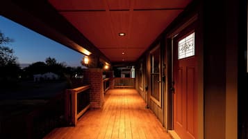 Une véranda en bois, recouverte et dotée d’un mur en briques et d’une balustrade en bois.