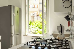 A kitchen with a gas stove, a refrigerator, and a window with a view of greenery.