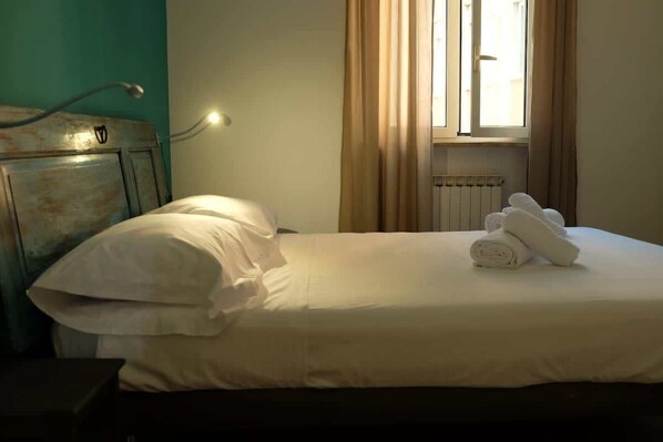 A neatly made bed with white linens, a rolled towel, and a bedside lamp.