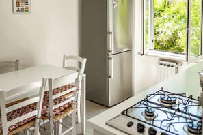 Une cuisine avec une table blanche, des chaises dotées de coussins à motifs, un réfrigérateur en acier inoxydable et une cuisinière à gaz.