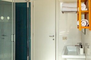 Een badkamer met een glazen douchecabine, een witte wastafel met spiegel en een handdoekrek met opgevouwen handdoeken.