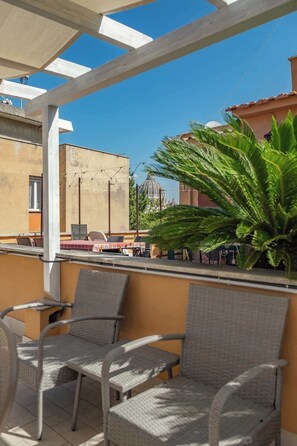 A balcony with wicker chairs, a palm tree, and a view of a building with a dome.