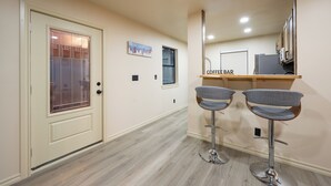 A modern kitchen with a coffee bar, two bar stools, and a door with a frosted glass panel. - Modern Cabin  Mins from TU, Downtown, Expo, St John and HIlcrest - upstairs (Tulsa)