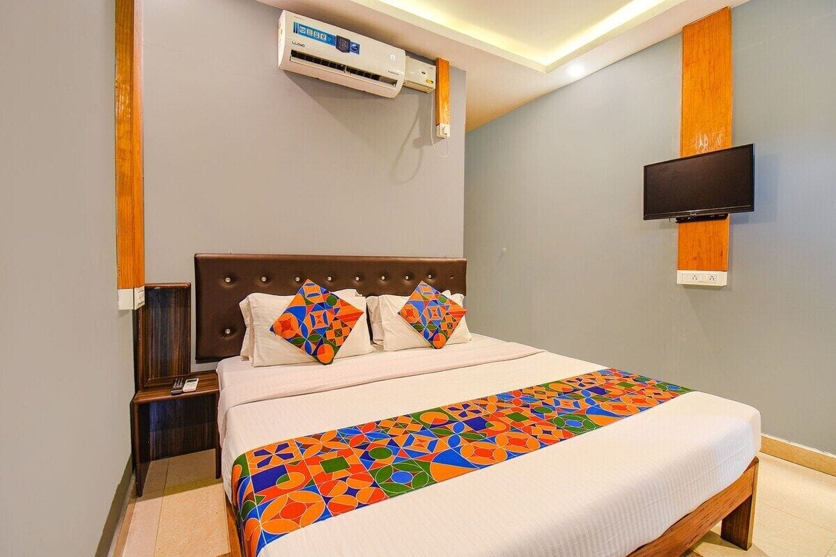 Habitación de hotel con cama, televisor montado en la pared y aire acondicionado sobre la cama.