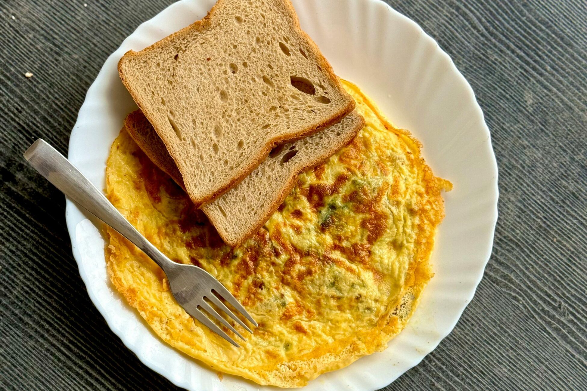 A plate with an omelette and two slices of bread on a white plate.