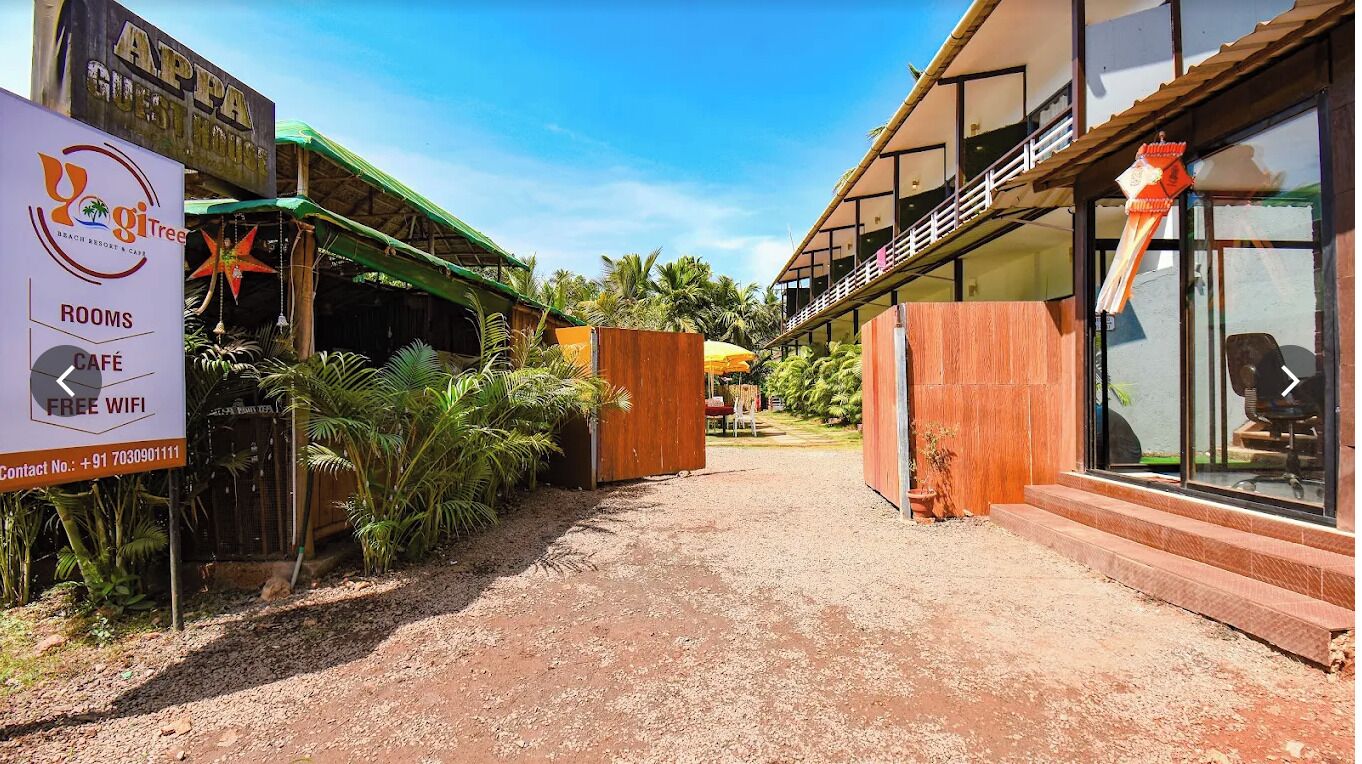 Uma passagem que leva a um edifício com a placa 'APPA GUEST HOUSE' e 'YogiTree Beach Resort & Spa'.