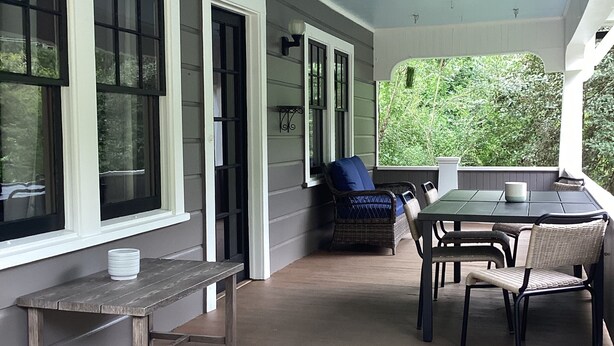 A covered porch with a table and chairs, a bench, and a window with a view of greenery.