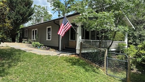A residential house with a porch, a flag, and a fenced yard.