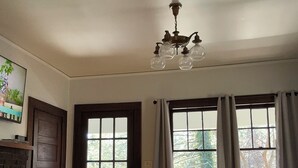A room with a fireplace, a table, a chair, a window with curtains, and a ceiling light fixture.