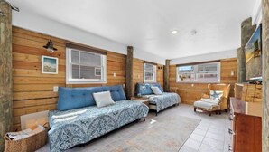Una habitación acogedora con paredes de madera, dos camas con ropa de cama estampada, una silla y una mesita.