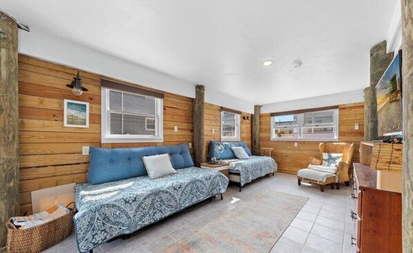 A cozy room with wooden walls, two beds with patterned bedding, a chair, and a small table.