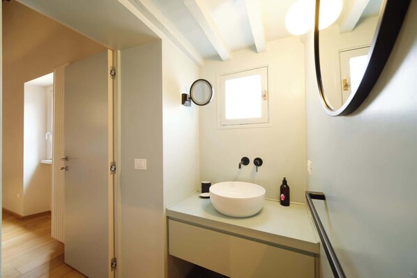 A bathroom with a white sink, a round mirror, and a window.