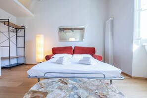 A hotel room with a bed, a red headboard, a bedside table, a lamp, a radiator, and a window.