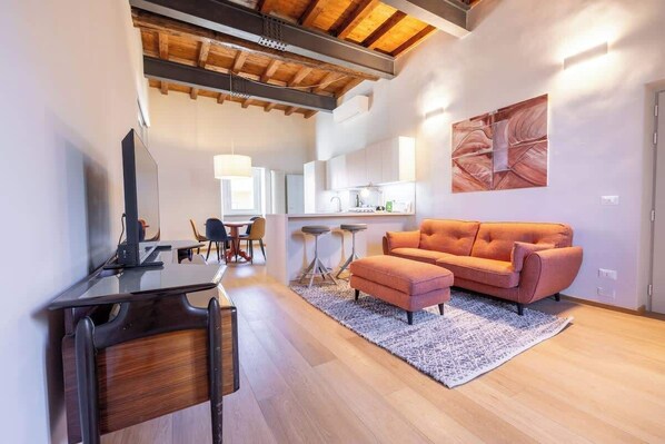A modern living room with a sofa, a desk, and a kitchen in the background.