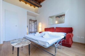 A room with a bed, a small table, a red chair, and a mirror on the wall.