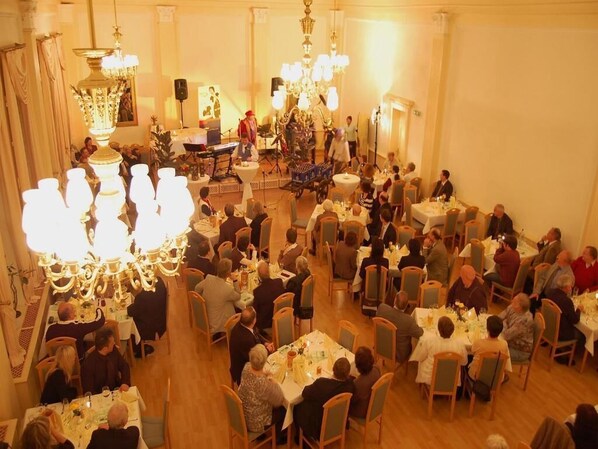 A large dining hall with multiple tables and chairs, chandeliers, and a band performing on stage. - Goldene Henne (Arnstadt)