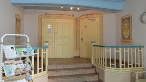 Ein Hotel Eingangsbereich mit einer Rezeption, zwei Türen und einer Treppe, die zu den oberen Stockwerken führt.