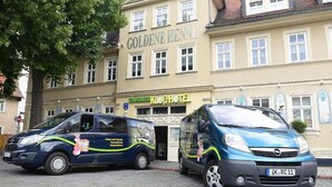 Zwei blaue Lieferwagen parken vor einem Gebäude mit der Aufschrift 'GOLDENE HENNE'.