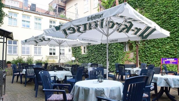 Ein Essbereich im Freien mit Tischen und Stühlen, beschattet durch Sonnenschirme mit 'Ur-Kröltiger'-Branding.