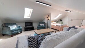 Ein modernes Schlafzimmer im Loft-Stil mit einem großen Bett, einer Couch, einem Fernseher und einem Schreibtisch.