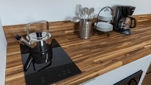 Eine Küchenarbeitsplatte mit einem schwarzen Induktionskochfeld, einem Wasserkocher, einer Kaffeemaschine und einer Besteckablage.