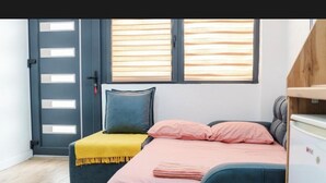 A small bedroom with a bed, a bench, a door, and a window.