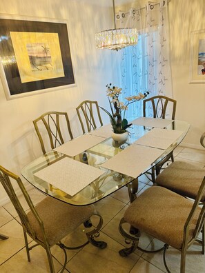 Un coin repas avec une table en verre, des chaises en osier, un vase de fleurs et un lustre.