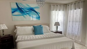 Ein Schlafzimmer mit Bett, einer Bank, einem Nachttisch, einer Lampe, einem Kronleuchter und einem Fenster mit Vorhängen.
