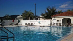 Ein Pool mit Liegestühlen und einer überdachten Liegefläche, umgeben von Gebäuden und Palmen.