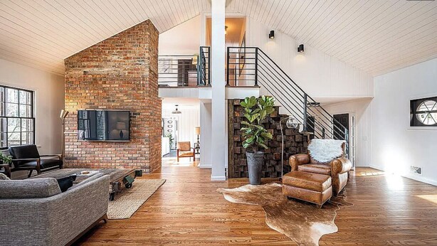 A spacious living area with a brick accent wall, a leather sofa, a large potted plant, and a wooden floor.