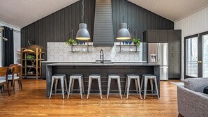 A modern kitchen with a central island, bar stools, and pendant lighting.