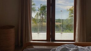 A bedroom with a large window, a bed, and a wicker basket.