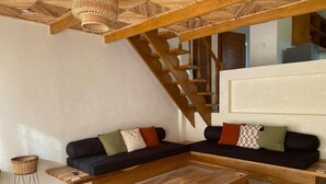 A modern living room with a wooden staircase, black sofas with patterned cushions, and a woven basket on a wooden table.
