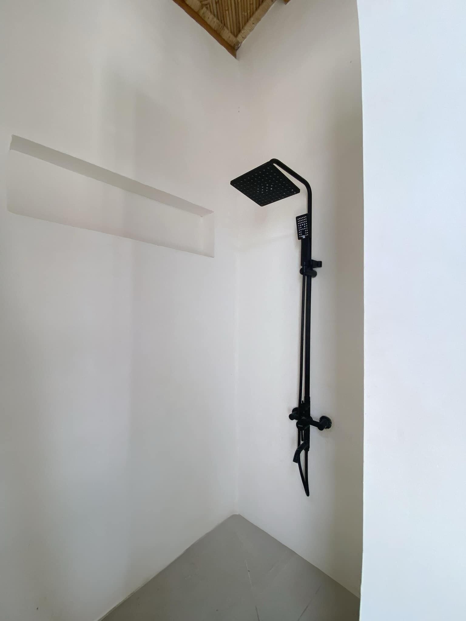Un baño pequeño con paredes blancas, cabezal de ducha negro y panel de control montado en la pared.