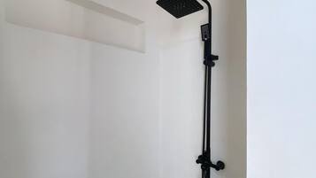 Un baño pequeño con paredes blancas, cabezal de ducha negro y panel de control montado en la pared.