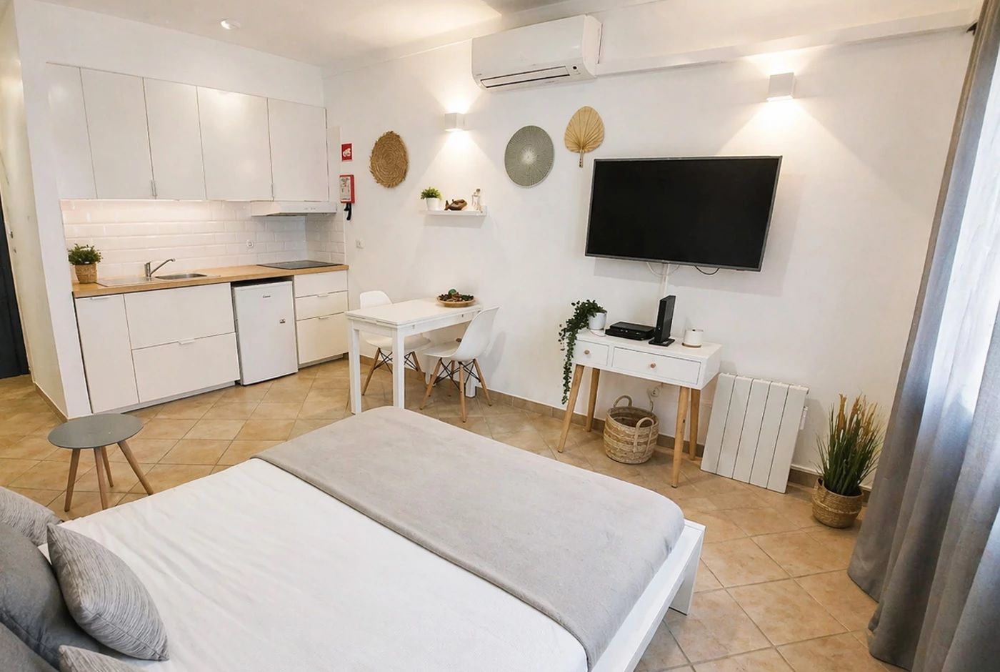 Habitación de hotel pequeña con kitchenette, una cama, un escritorio y un televisor.