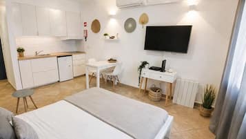 Habitación de hotel pequeña con kitchenette, una cama, un escritorio y un televisor.