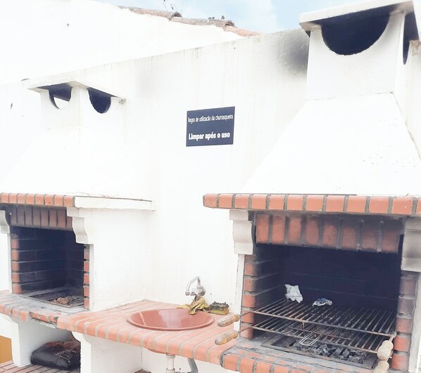 An outdoor kitchen area with two brick ovens, a sink, and a sign instructing to clean after use. - Mira Vila Studio - Duna Parque Resorts & Hotels (Odemira)