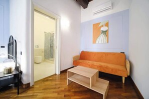 Una habitación con piso de madera, un sofá, una mesa de centro, un cuadro en la pared y una puerta que da a un baño.