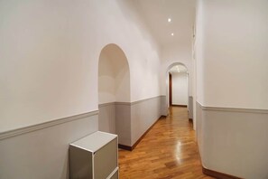 A corridor with white walls and wooden flooring, leading to an arched doorway.