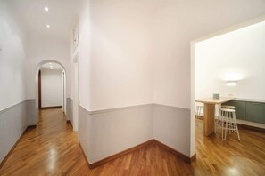 A corridor with wooden flooring leading to a kitchen area with a table and stools. - BuddyRent - Dadada - Trevi - 8 ospiti (Roma)