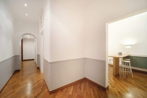 Un pasillo con piso de madera que conduce a una zona de cocina con una mesa y taburetes.