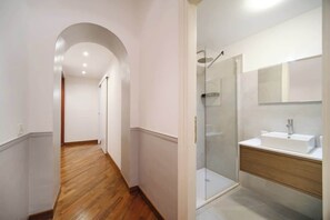 A hallway with wooden flooring, a glass shower enclosure, and a white sink with a wooden vanity. - BuddyRent - Dadada - Trevi - 8 ospiti (Roma)